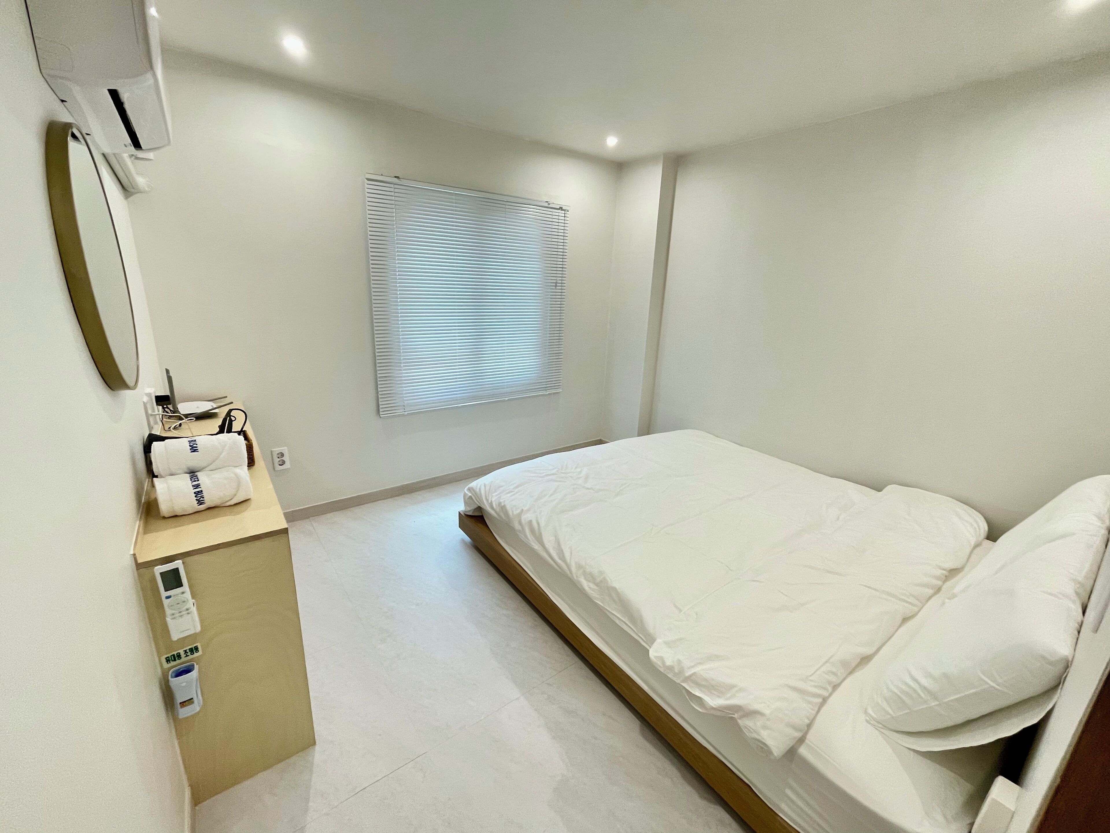 Et moderne hotelværelse med en seng, et lille skrivebord med en computer og et vindue med persienner.