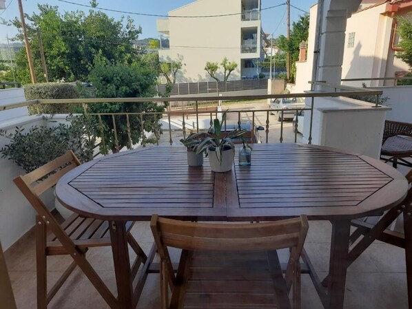 Een ronde houten tafel met stoelen op een balkon, omringd door plantenpotten en met uitzicht op een woonwijk.