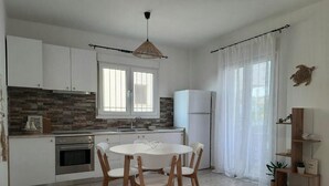 A modern kitchen with white cabinets, a brick backsplash, and a dining area with a round table and wooden chairs. - Live your summer days at Kyveli's Residence (Nikiti)