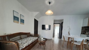 A living room with a sofa, a dining table with chairs, a TV mounted on the wall, and a wooden floor. - Live your summer days at Kyveli's Residence (Nikiti)