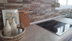 A kitchen with a stone backsplash, a stainless steel sink, and a woven basket containing bottles. - Live your summer days at Kyveli's Residence (Nikiti)