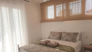A bedroom with a bed, pillows, a bedside table, and a window with blinds. - Live your summer days at Kyveli's Residence (Nikiti)