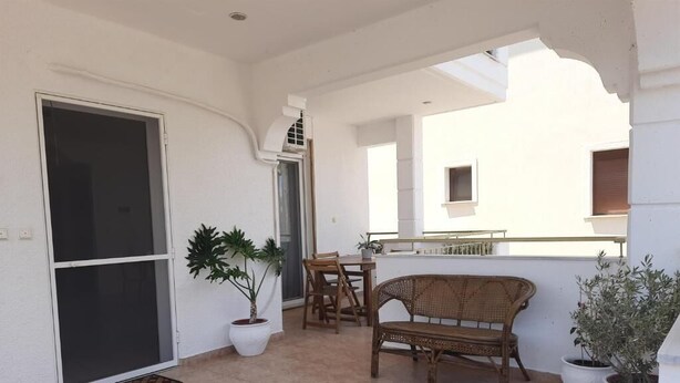 A balcony with a sliding door, a wicker bench, a table, and potted plants. - Live your summer days at Kyveli's Residence (Nikiti)