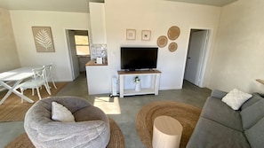 A modern living room with a TV, white furniture, and a dining area. - WHALES AND BALES, BREMER BAY — A UNIQUE RETREAT WITH SERENITY & OCEAN VIEWS (Bremer Bay)
