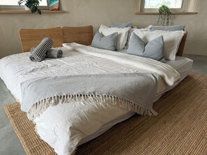 Una cama con cabecera de madera, varias almohadas, una colcha blanca y una alfombra tejida.