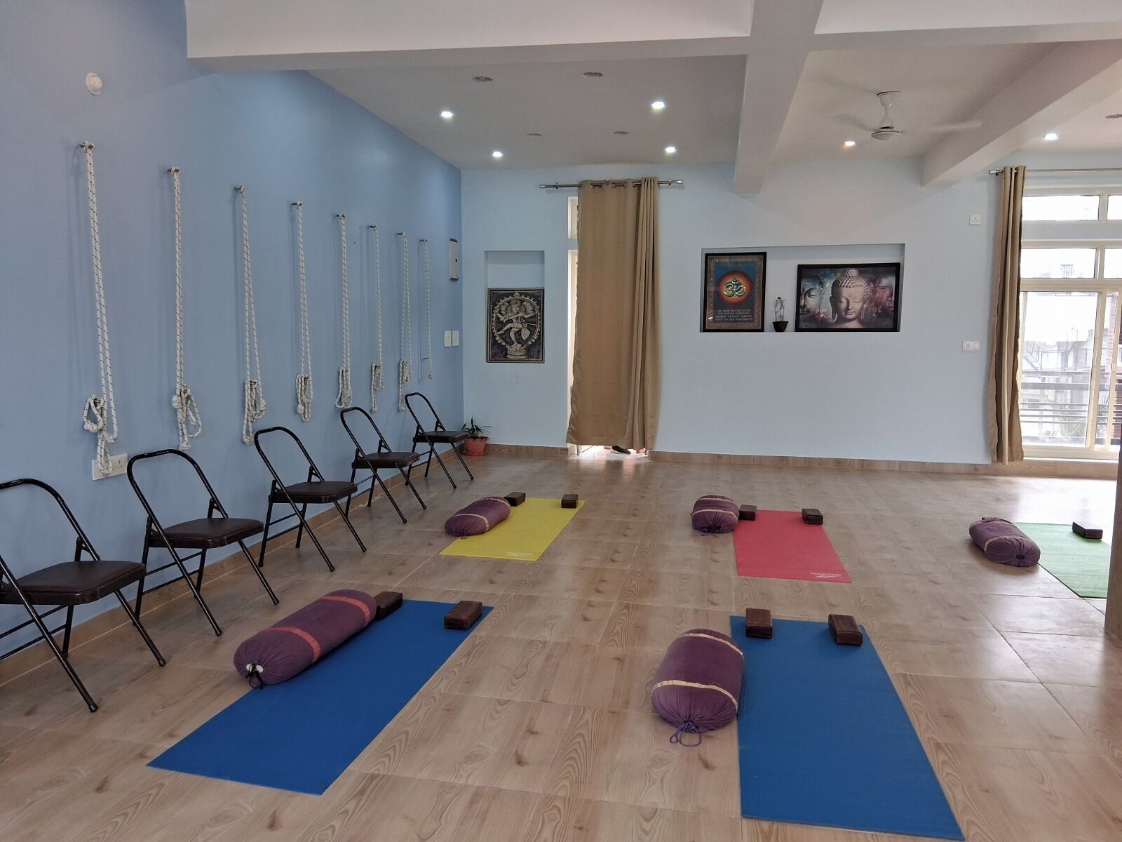 Un estudio de yoga con pisos de madera, paredes azules y un ventanal grande.