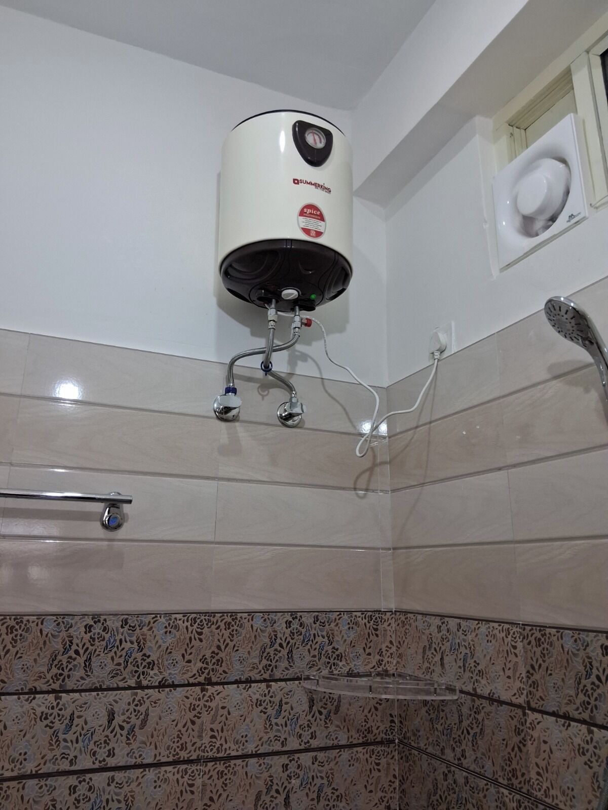 A bathroom with a white water heater mounted on the wall, a showerhead, and a towel rack.