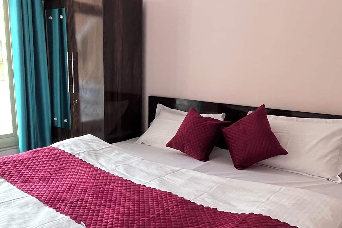 A neatly made bed with a white and red quilt, a dark wooden wardrobe, and a framed landscape painting on the wall.