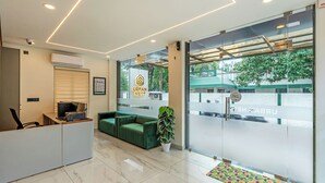 Egy modern irodai tér, amelyben található egy fogadótér, zöld színű ülőgarnitúrák, valamint egy nagy ablak, melyből zöld növényzetre és egy épületre nyílik kilátás.