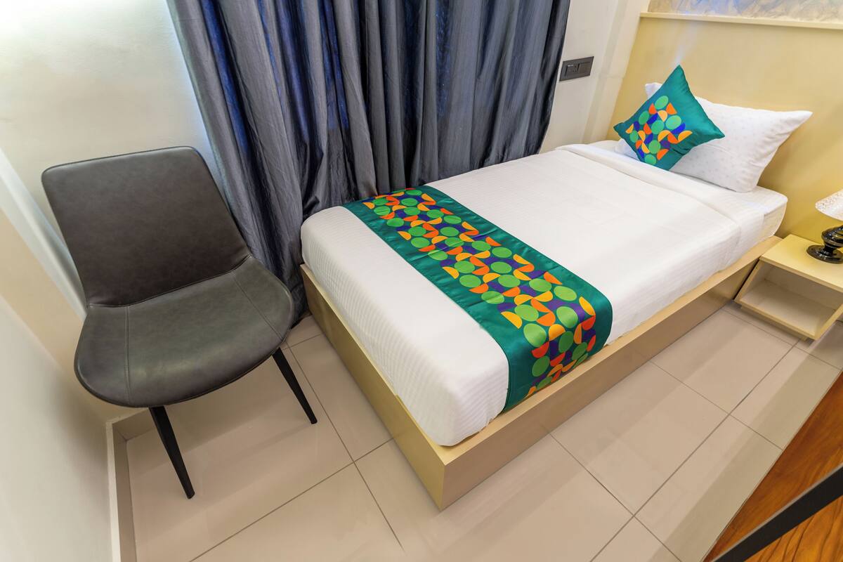 Una habitación de hotel con una cama, una silla, una mesita de noche y una cortina.