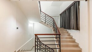 Egy modern lépcső, fa korláttal és fém oszlopokkal, amely egy pihenőhelyre vezet, ahol sötét függöny van.