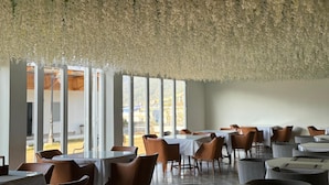 A restaurant with tables and chairs, large windows, and hanging floral decorations. - Namdul Retreat (Mangan)