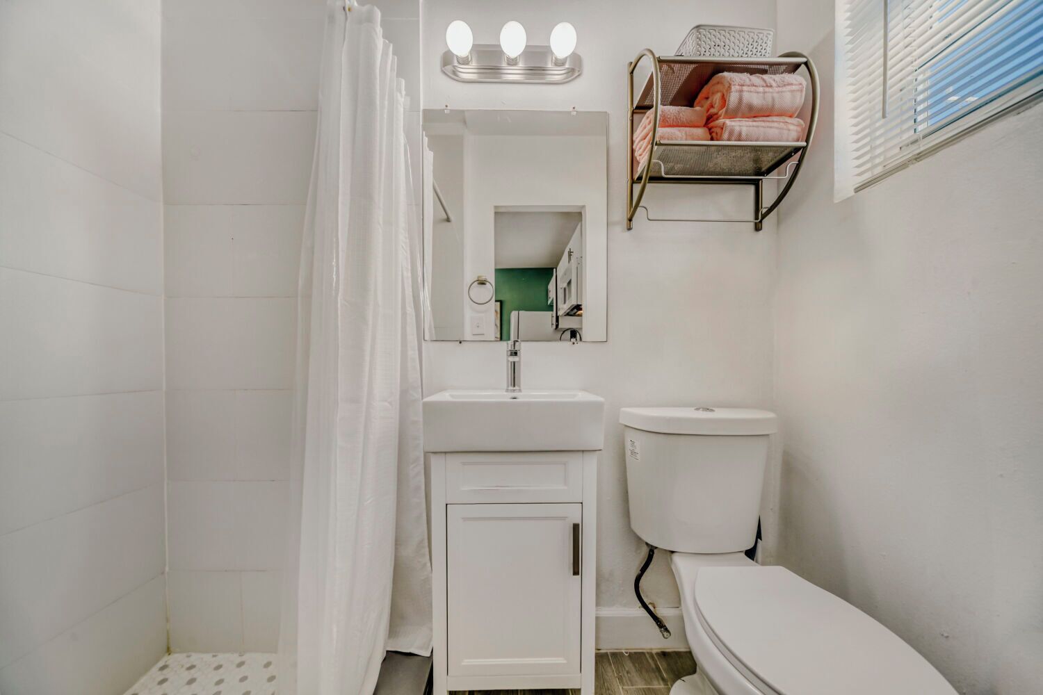 Een badkamer met douchegordijn, wastafel, toilet en een spiegel met verlichting.