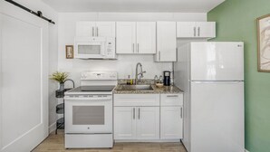 A compact kitchen with white cabinets, a microwave, an oven, a sink, and a refrigerator. - 2528 Renovated Studio Near The Beach (Melbourne)