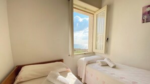 A room with two beds, a window with a view of the sea, and a wall-mounted picture. - Beautiful home with panoramic sea view (borders state property) (Marina di Mancaversa)