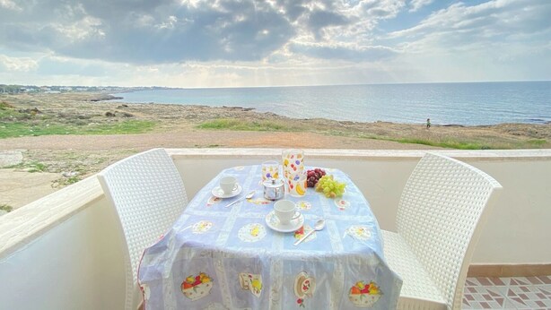A table set for two with a view of the sea and a cloudy sky. - Beautiful home with panoramic sea view (borders state property) (Marina di Mancaversa)