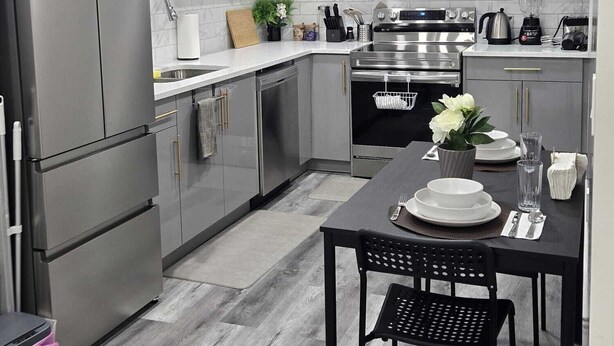 Una cocina moderna con gabinetes grises, electrodomésticos de acero inoxidable y una zona de comedor con una mesa dispuesta para dos personas.