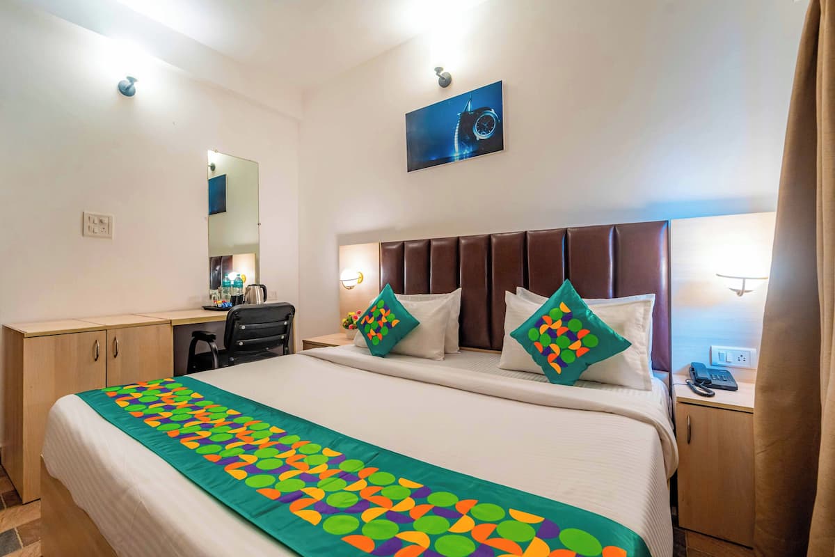 A hotel room with a large bed, a desk, a chair, a mirror, and a nightstand with a phone.
