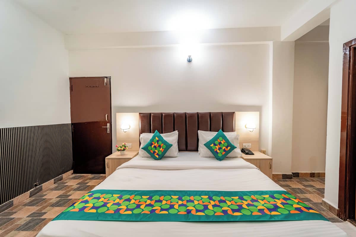 A hotel room with a large bed, two bedside tables with lamps, a wooden wardrobe, and a patterned bedspread.