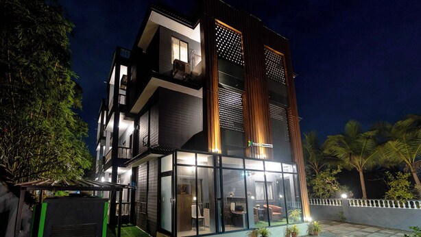 A modern multi-story building with a glass facade, outdoor seating area, and a visible balcony. - Treebo Clarissa Resort with Swimming Pool (Saligao)