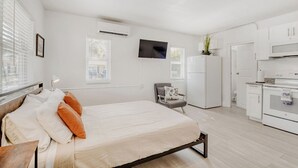 Een moderne slaapkamer met een bed, een bureau, een stoel, een televisie en een keukenhoek.