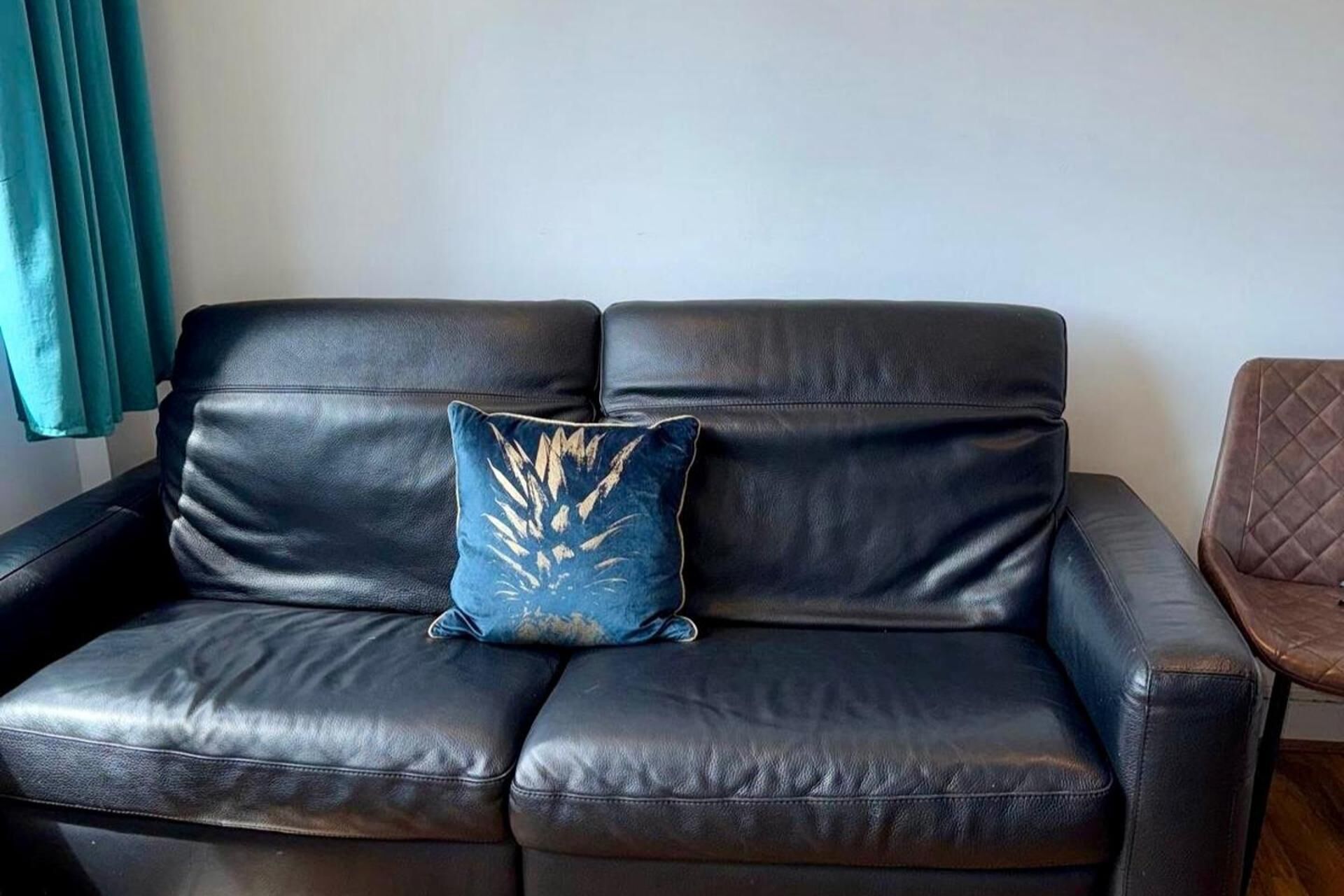 A black leather sofa with a single blue pillow with a leaf pattern.