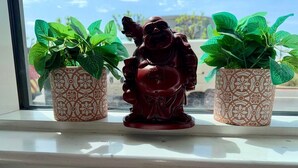 Egy ablakpárkány, rajta két mintás virágcserep és egy Buddha-szobor.