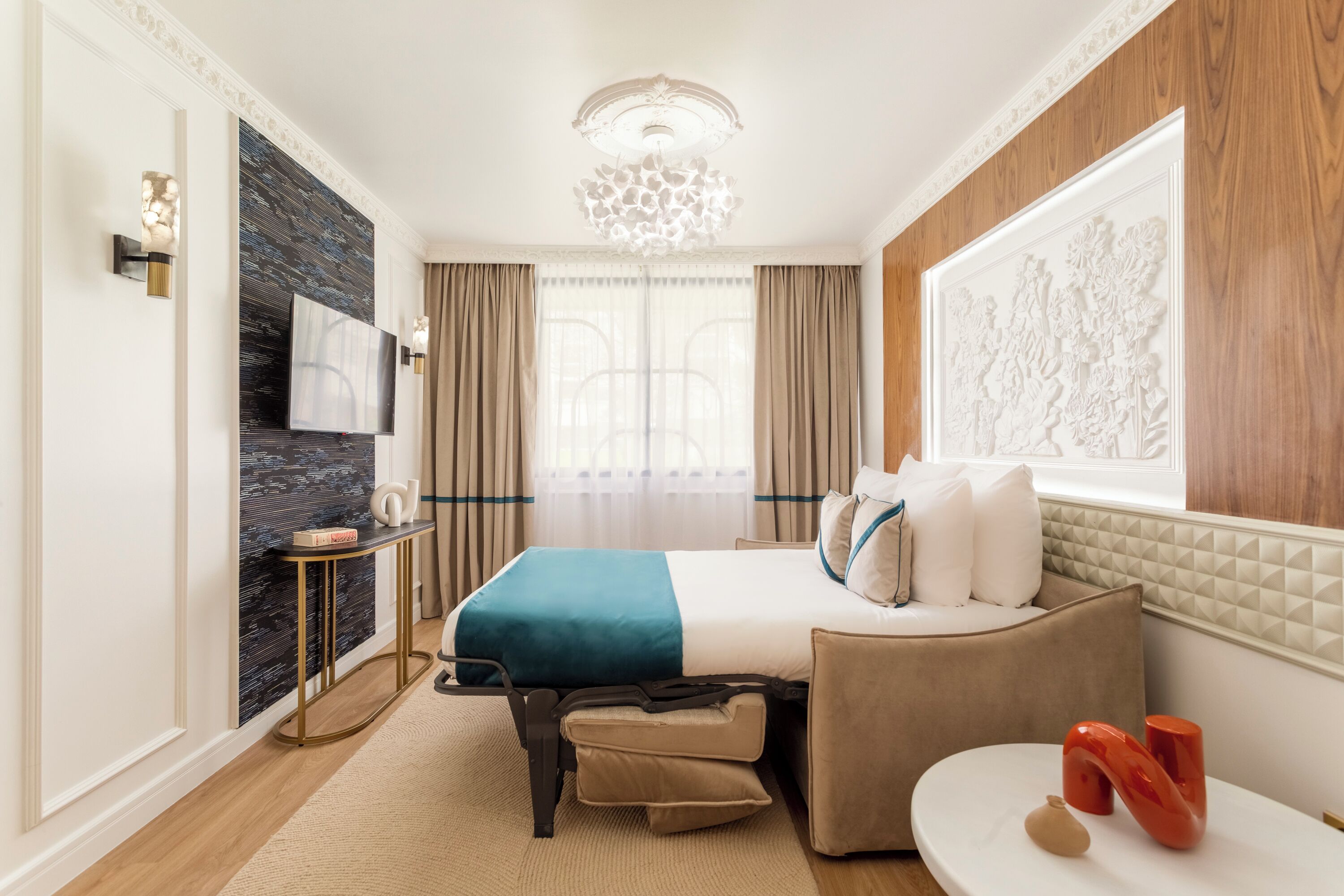 A modern hotel room with a large bed, a sofa, a desk, and a TV.