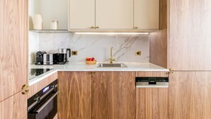 Una cocina moderna con armarios de madera, encimera de mármol, horno empotrado, cafetera y frutero.