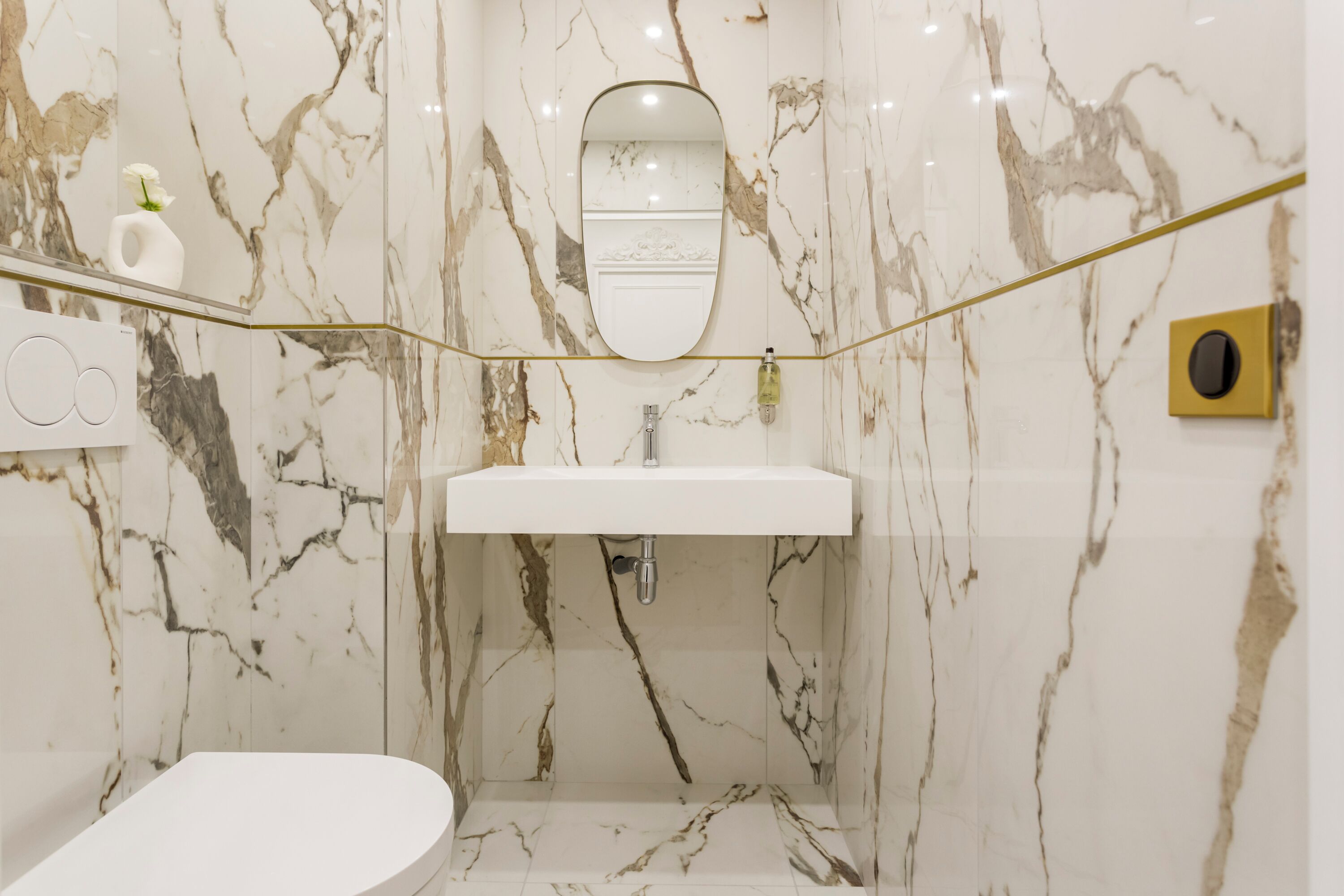 A bathroom with a marble wall, a white sink, a mirror, and a toilet.
