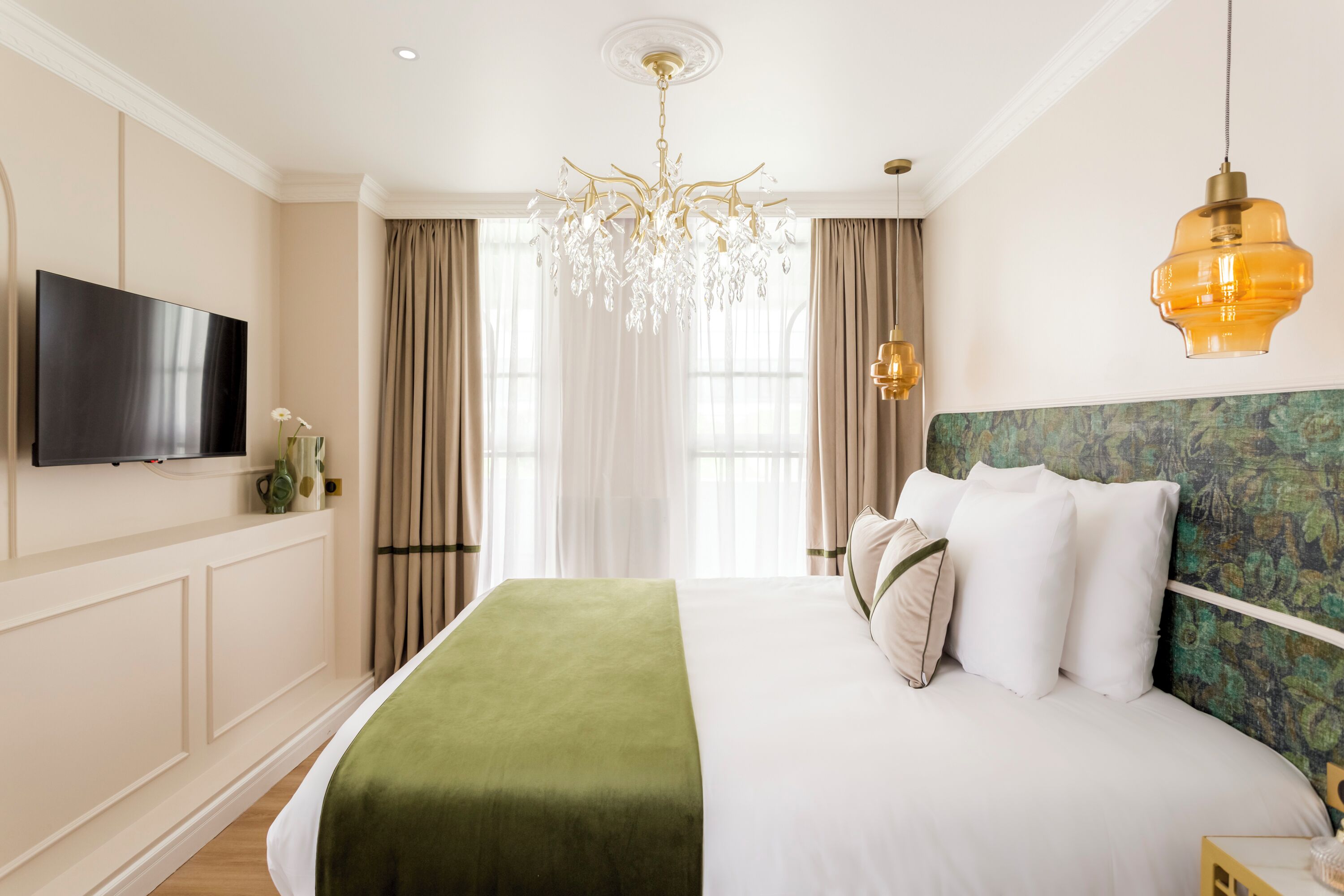 A hotel room with a large bed, a television, a chandelier, and a view of the outdoors.