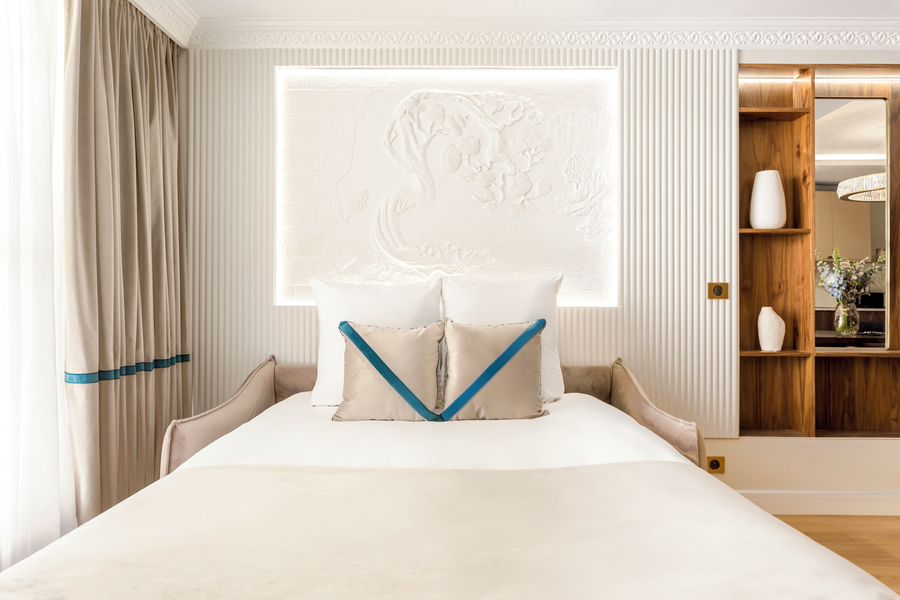 Una camera d'albergo con un letto grande, una testiera decorativa e un mobile contenitore in legno con uno specchio.