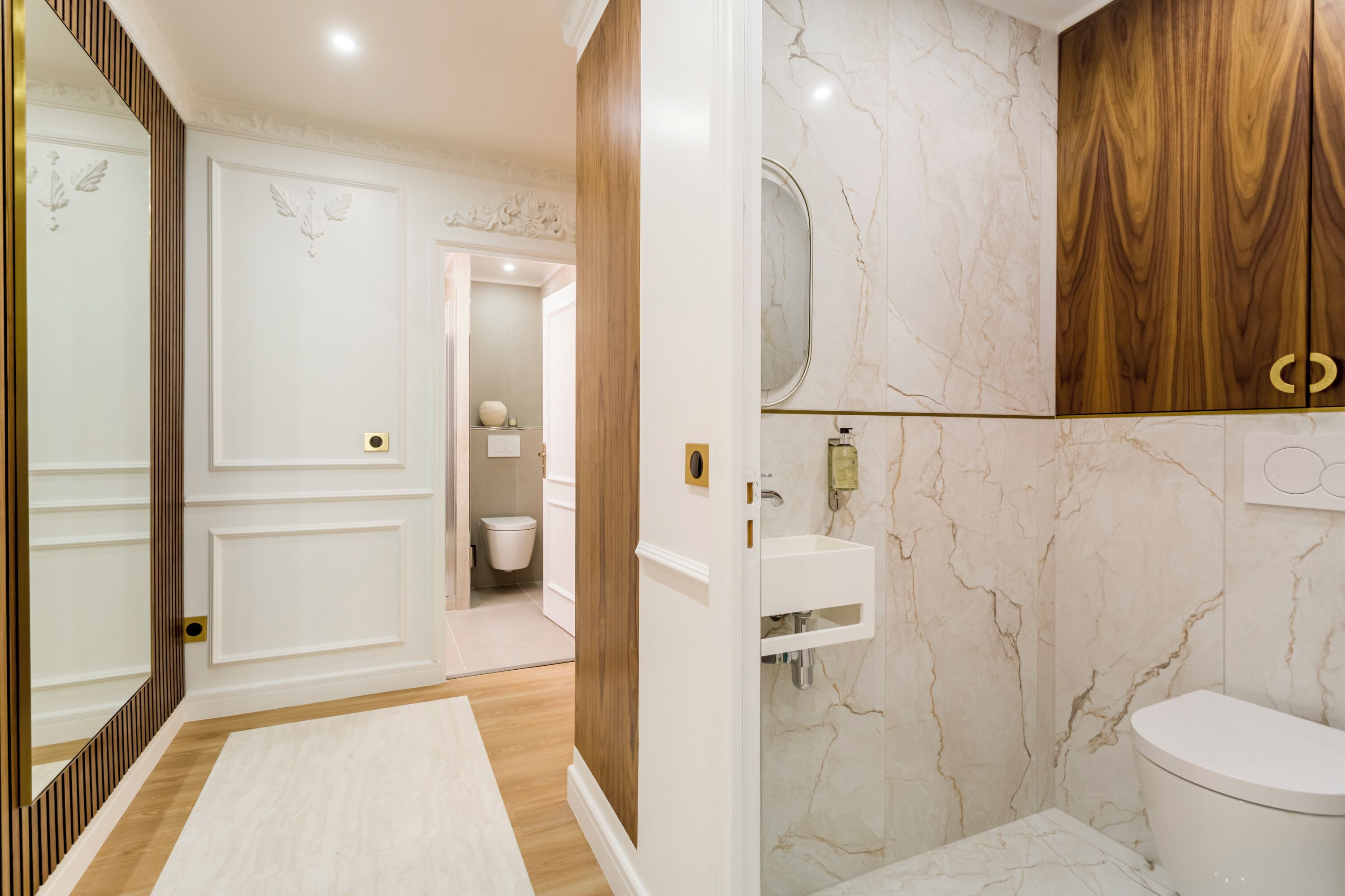 Une salle de bain moderne avec un mur en marbre, un meuble-lavabo en bois et des toilettes blanches.