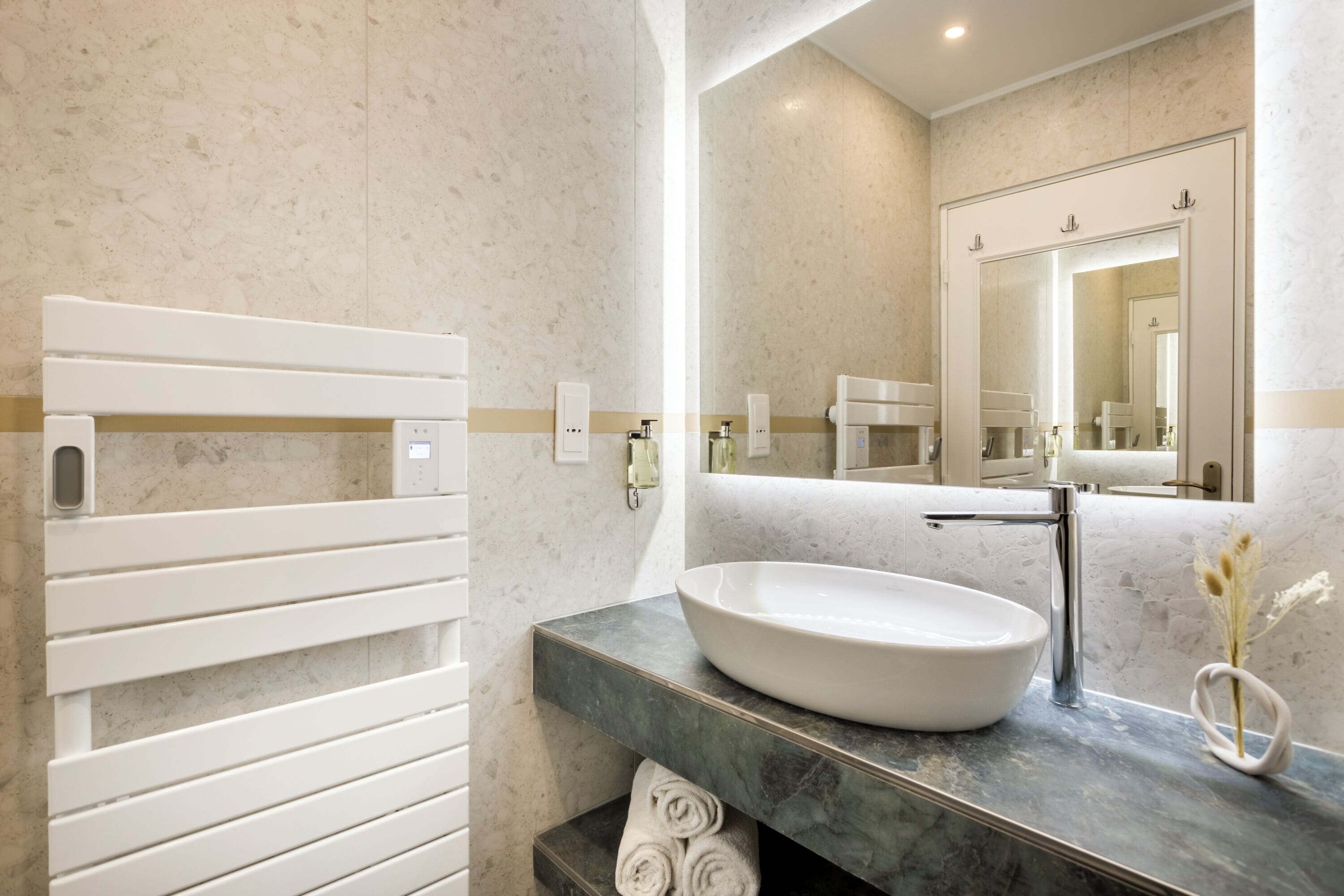 Un baño moderno con lavamanos blanco, encimera de mármol y toallero.