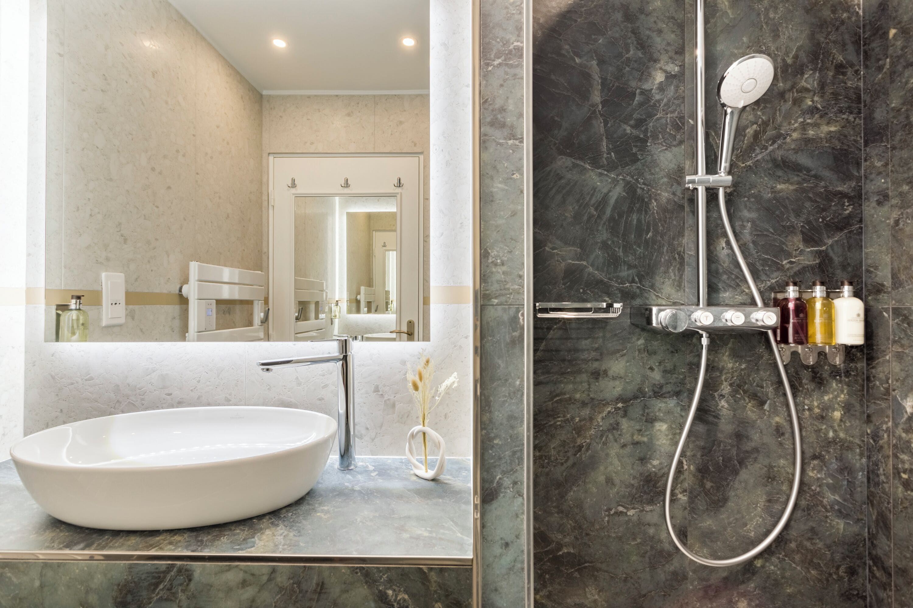 Een moderne badkamer met een groot ovaal wastafel, een handdouche en een douchecabine betegeld met marmer.