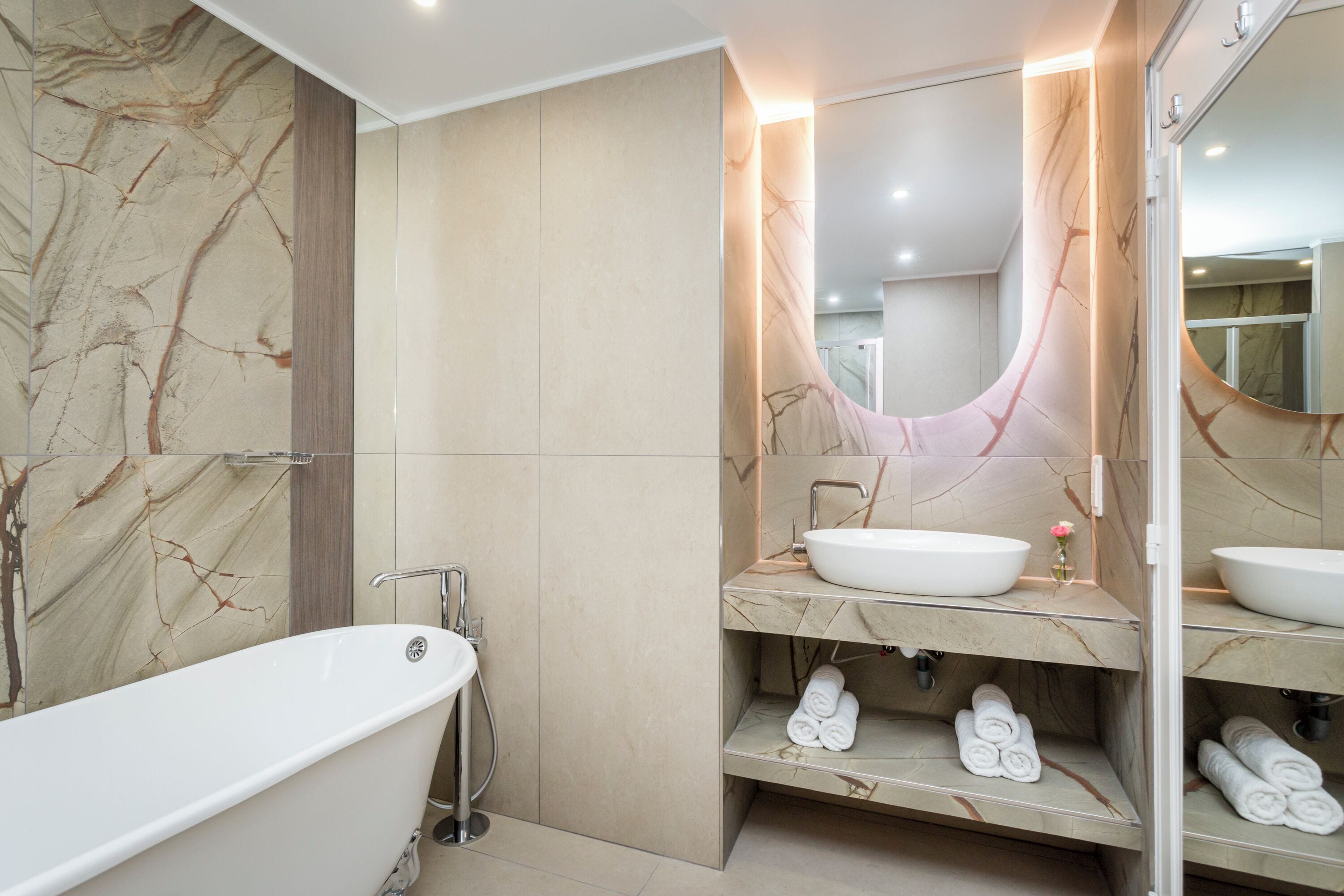 Een moderne badkamer met een vrijstaand bad, een grote spiegel en marmeren wanden.