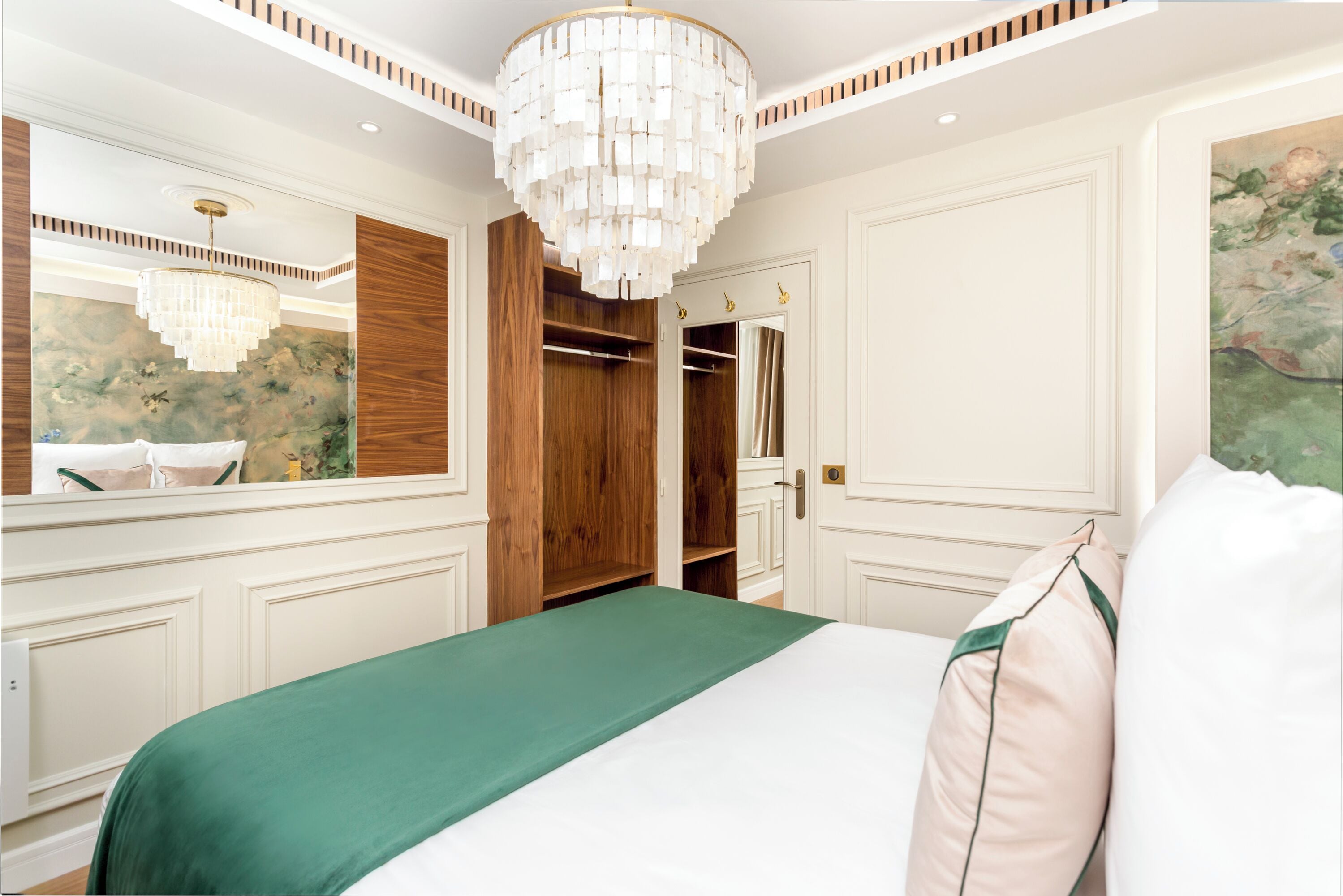 A bedroom with a large bed, a wooden wardrobe, a mirror, and a chandelier.