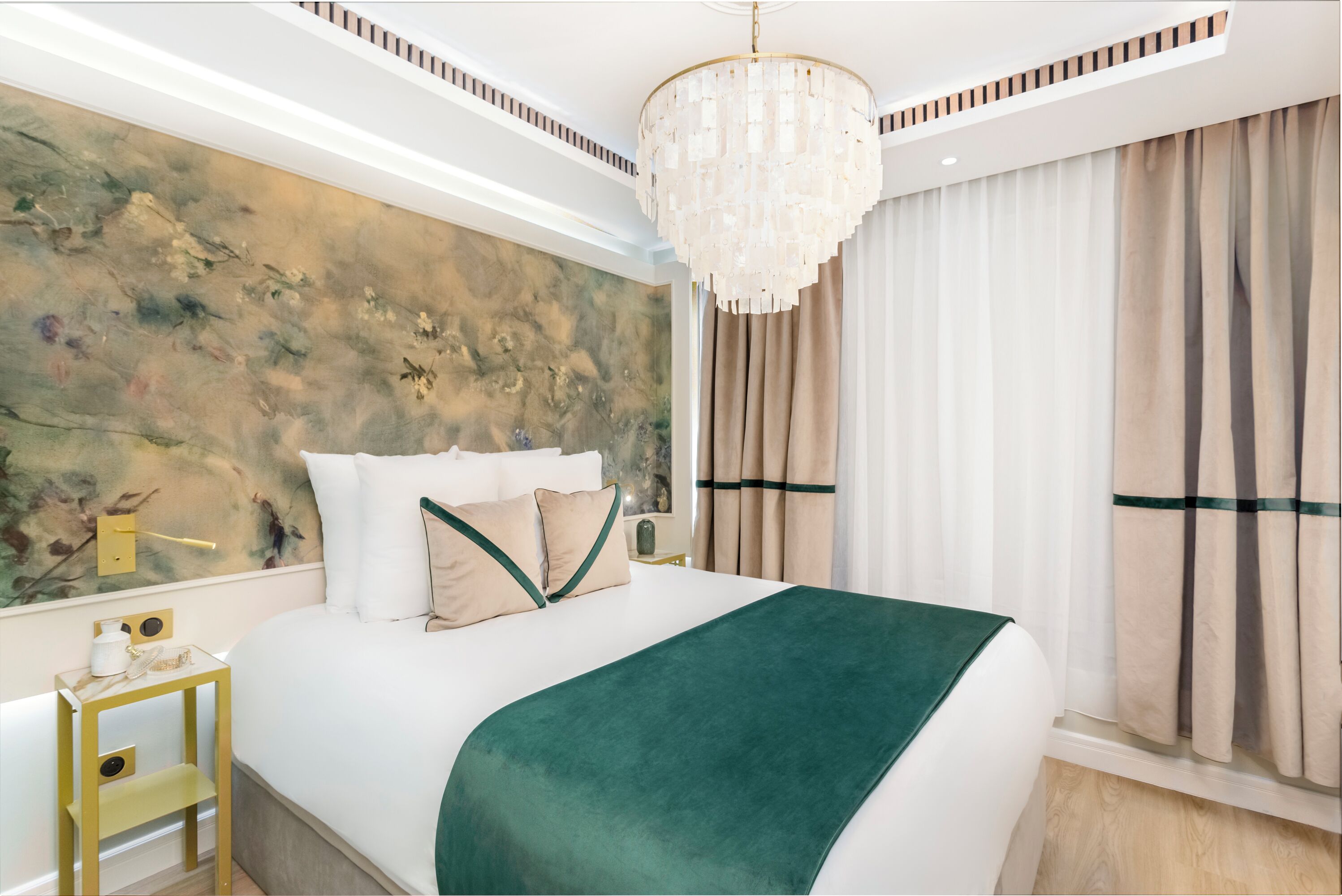 A bedroom with a large bed, a chandelier, a wall-mounted light, and a window with curtains.