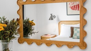 A bedroom with a wooden-framed mirror, a bedside lamp, a bed with pillows, and a framed artwork on the wall. - Bianca's- Stunning, Stylish & Steps from the Beach (Byron Bay)