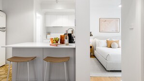 A modern kitchen with white cabinets, a central island with stools, and a coffee machine. - Bianca's- Stunning, Stylish & Steps from the Beach (Byron Bay)