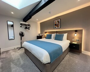 Een moderne slaapkamer met een groot bed, een plafondventilator, een nachtkastje met een lamp en een kunstwerk aan de muur.