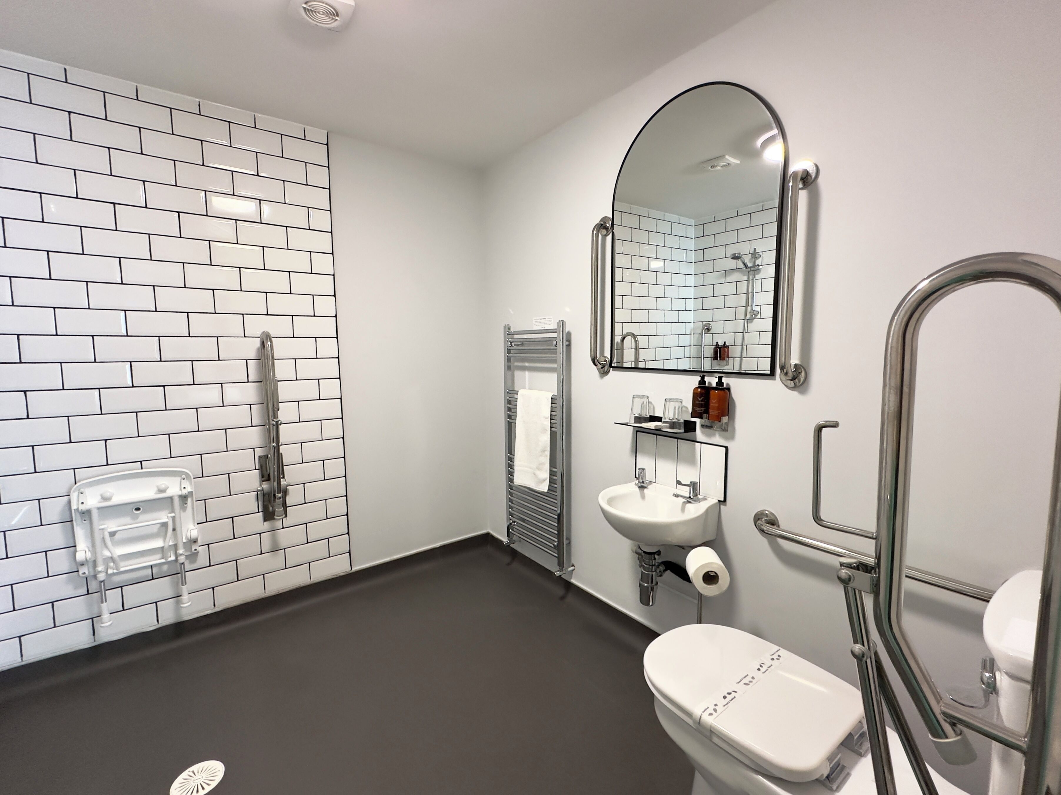 A modern bathroom with white subway tiles, a white sink, a toilet, a shower, and a mirror.