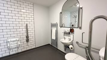 A modern bathroom with white subway tiles, a white sink, a toilet, a shower, and a mirror.