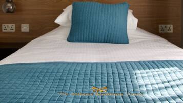 A neatly made bed with a blue quilt, a wooden headboard, and a framed artwork above it.