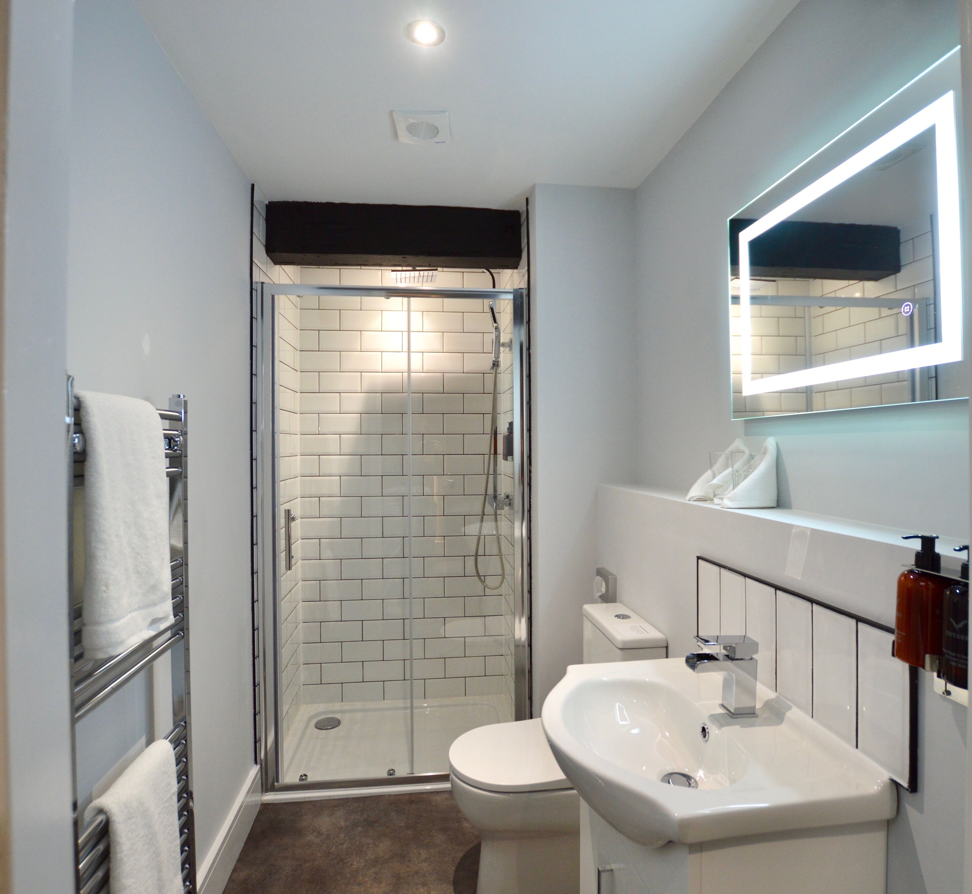 Un baño moderno con ducha de vidrio, inodoro blanco y lavamanos con espejo.