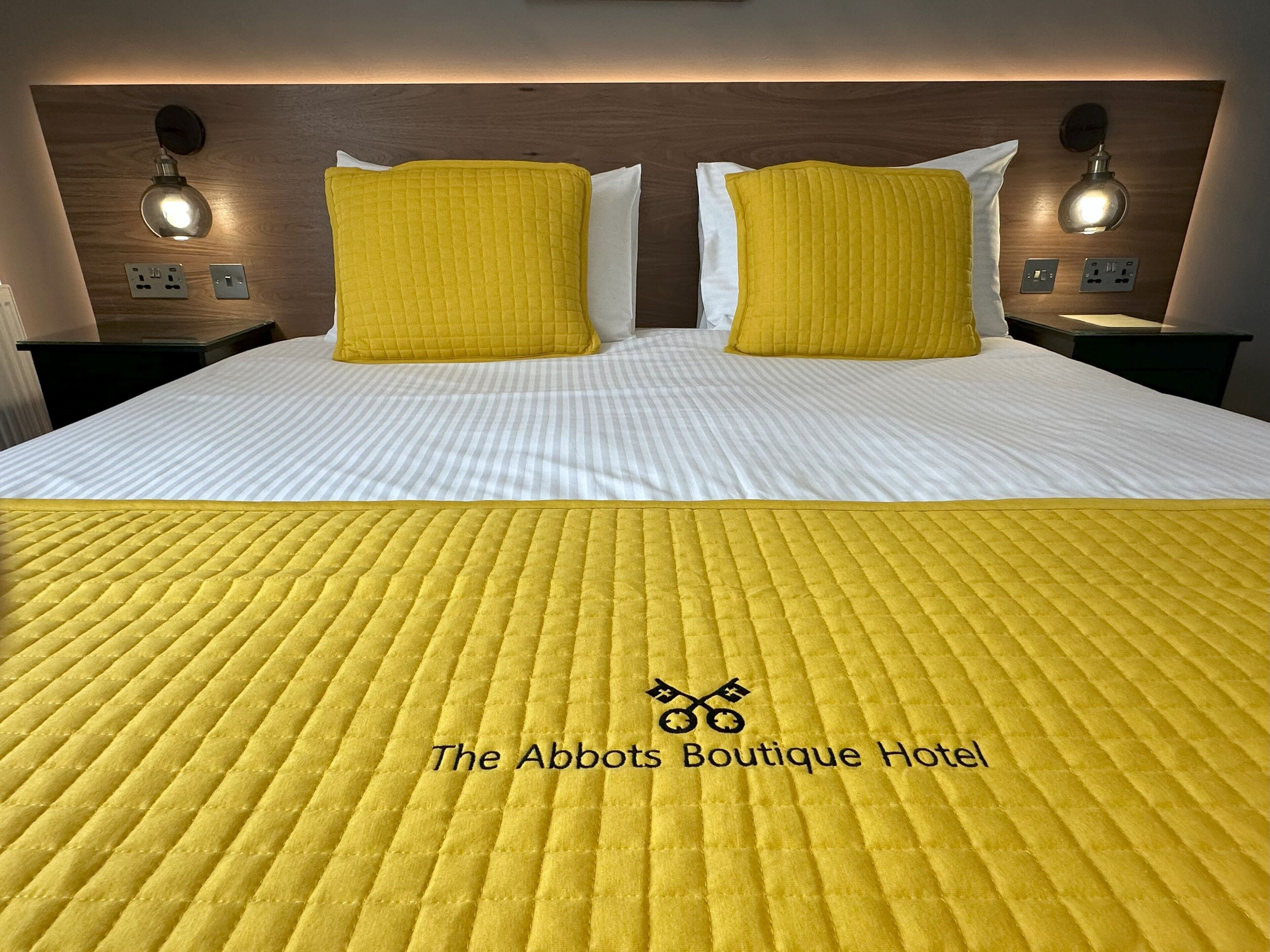 A hotel room with a bed, two bedside lamps, and a yellow quilted bedspread.