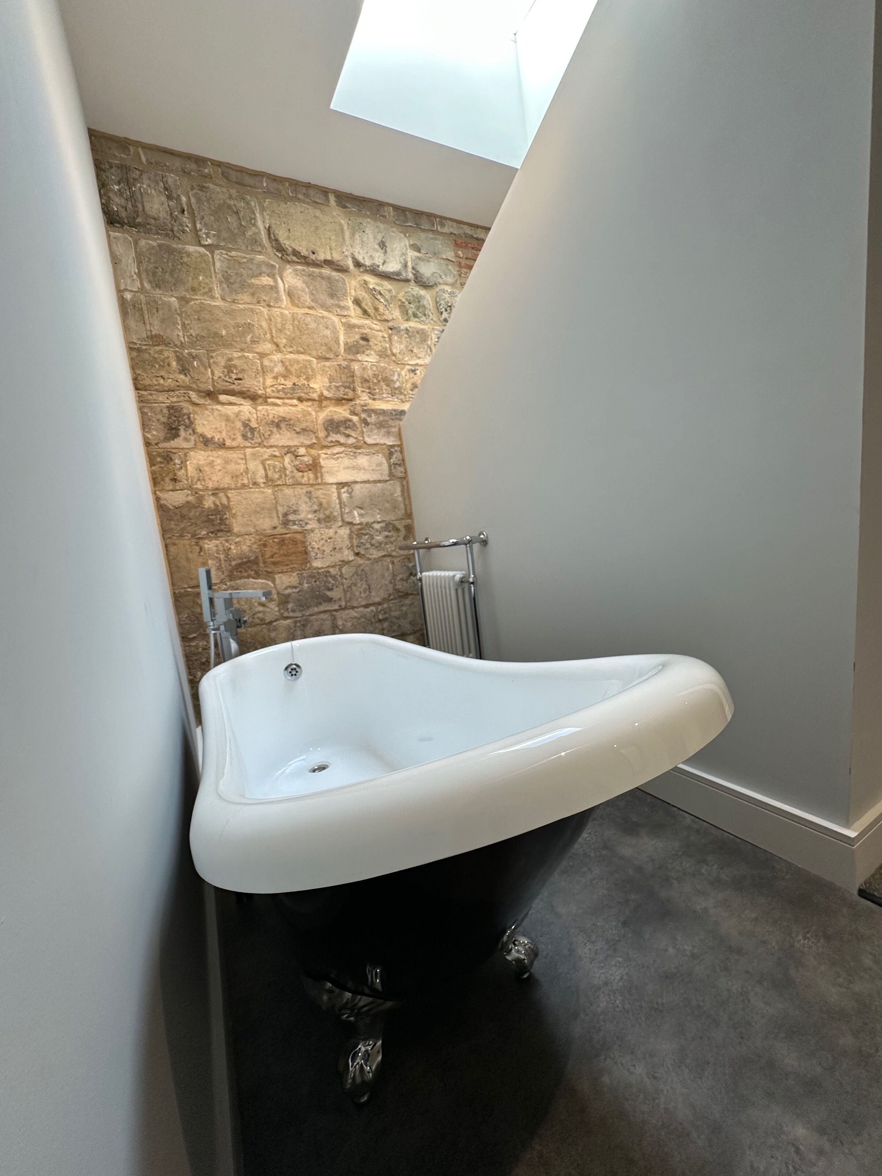 Un baño en esquina con pared de piedra, bañera blanca y radiador.