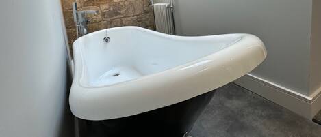 Un baño en esquina con pared de piedra, bañera blanca y radiador.