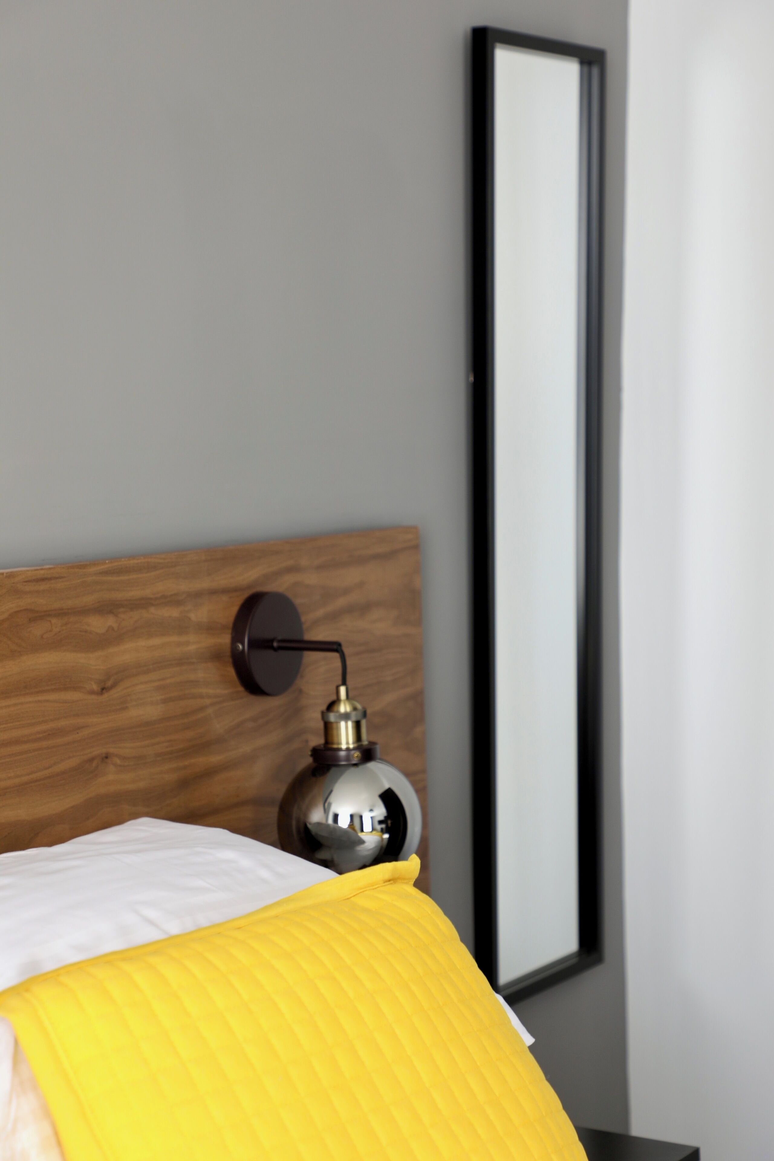 A bed with a wooden headboard, a bedside lamp, and a large mirror on the wall.