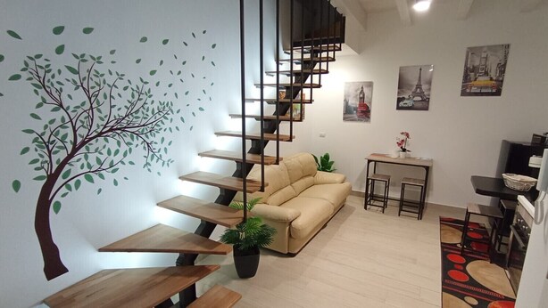 Una sala de estar moderna con una escalera en espiral, un sofá beige, una mesita con una planta y una mesa de centro.